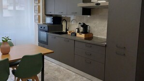 Et moderne køkken med lysegrå skabe, indbygget mikroovn og kaffemaskine. Der er et spisebord med stole og en potteplante på bordet.