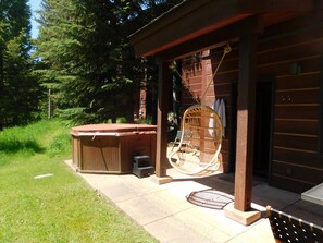 Une cabane en bois dotée d’un bain à remous, d’un fauteuil suspendu et d’un patio couvert.