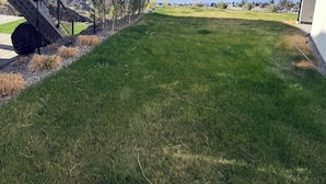 Un césped con una escalera que lleva a una zona cubierta, y una vista de un lago y montañas al fondo.
