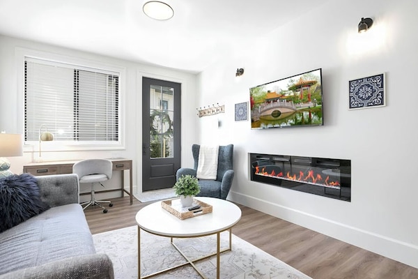 Living room with big screen smart tv, electric fireplace, office desk, window.