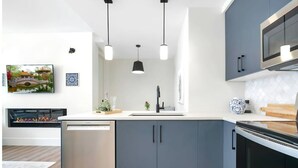 Una cocina moderna con armarios grises, un lavavajillas de acero inoxidable, un microondas y un horno empotrado. Hay luces colgantes sobre el fregadero y una pequeña planta en maceta en la encimera.