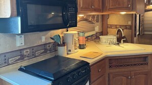 A compact kitchen with wooden cabinets, a black microwave, a stove, and a sink. - Cozy 1-bedroom Rv with pool,WiFi, AC in pleasant Elephant Butte (Elephant Butte)