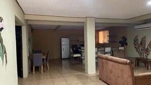 A spacious living area with a dining table and chairs, a sofa, and a refrigerator in the background.