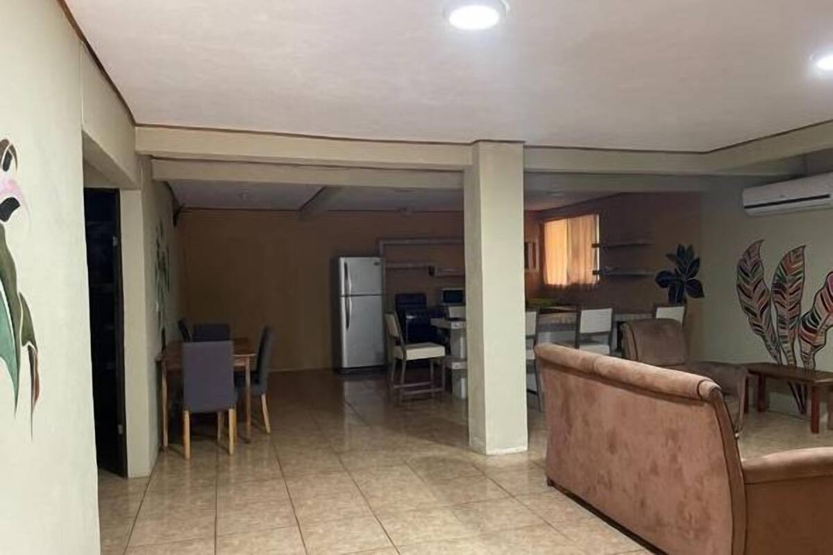 A spacious living area with a dining table and chairs, a sofa, and a refrigerator in the background.