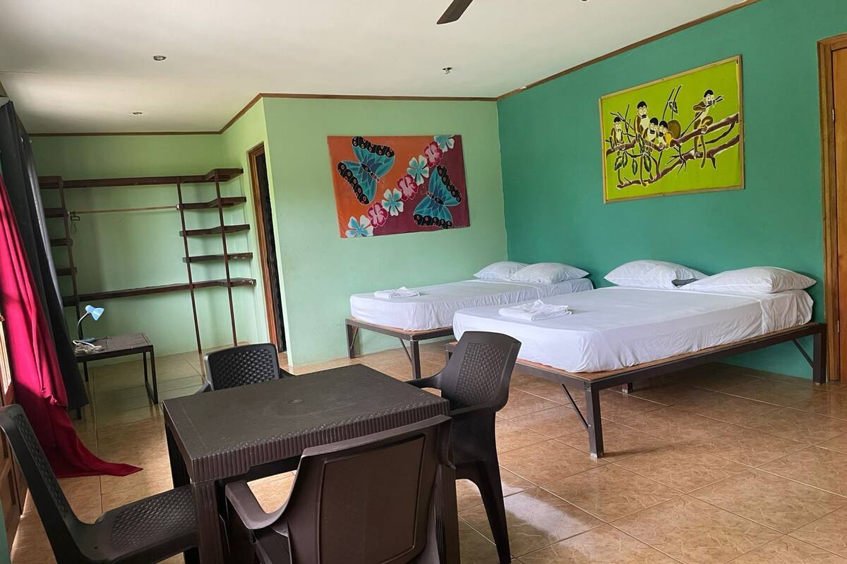 A room with two beds, a desk, and a chair. There are two paintings on the walls.