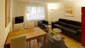 A modern living room with a wooden dining table, two sofas, a TV, and a glass coffee table.