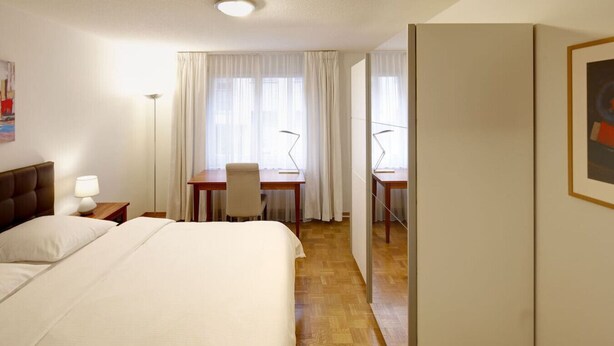 A hotel room with a bed, a desk, a chair, and a wardrobe.