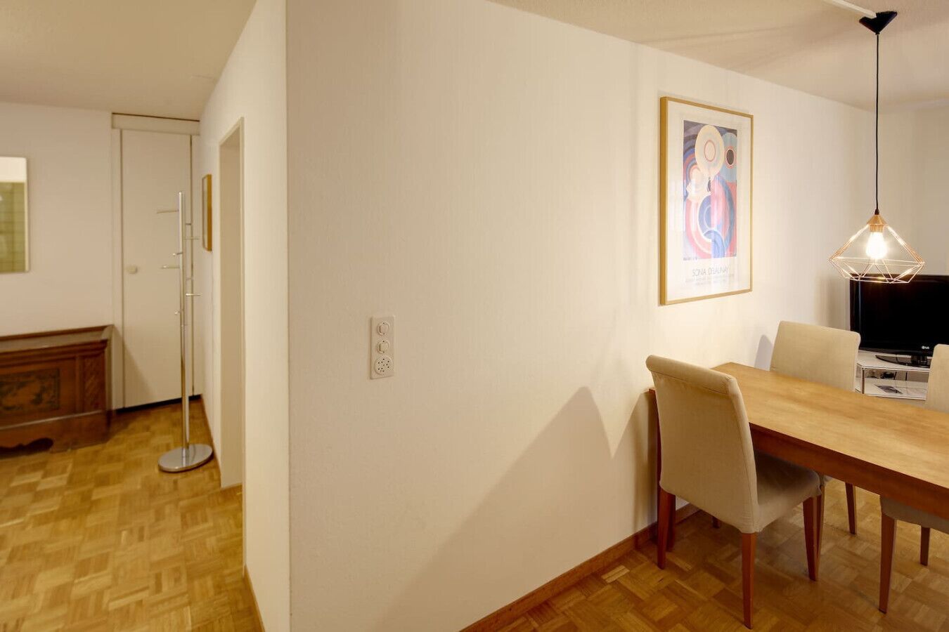 A dining area with a wooden table and chairs, a floor lamp, and a television.