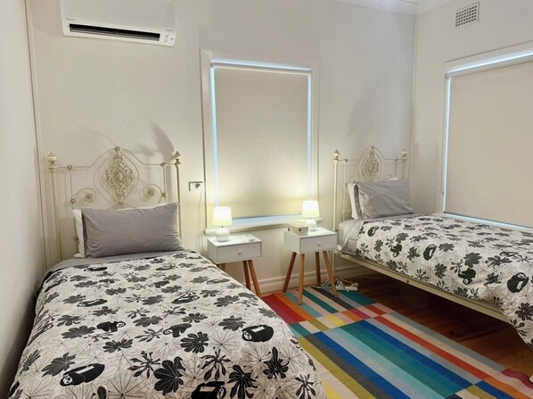 A bedroom with two beds, each with a floral bedspread, a bedside table with a lamp, and a mirror above the bed.
