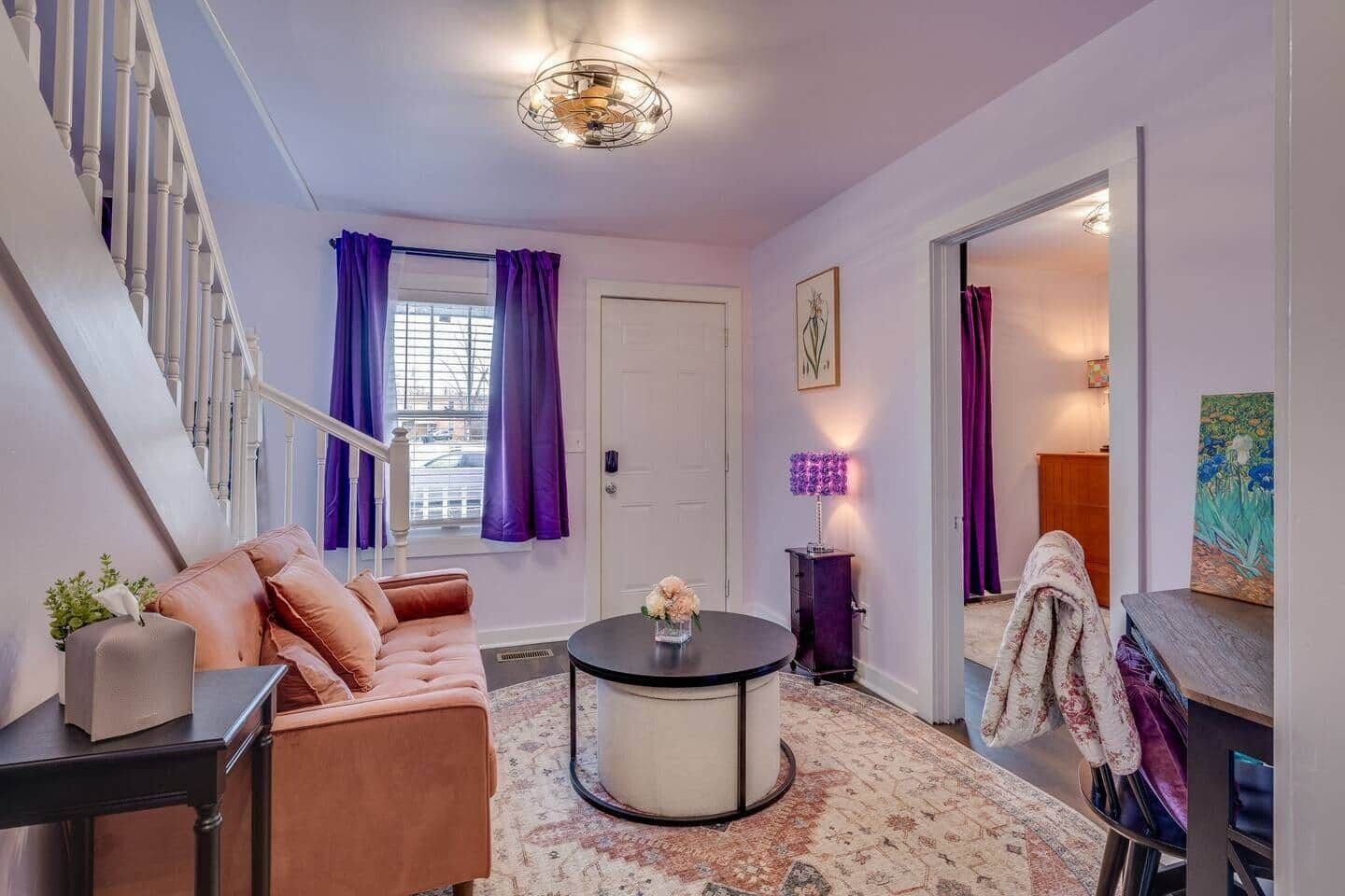A living room with a staircase, a round coffee table, a sofa, and a door leading to another room.