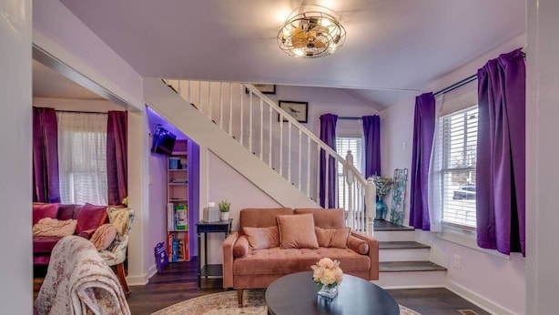 Ein Wohnzimmer mit Treppe, Sofa, Couchtisch und violetten Vorhängen.