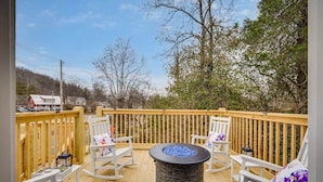Eine Holzterrasse mit weißen Schaukelstühlen und einem zentralen Feuerkorb.