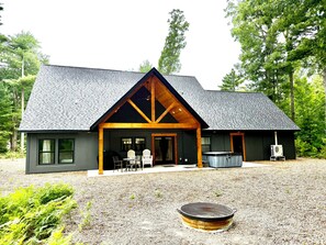 A modern house with a covered patio, outdoor seating, and a fire pit. - Cranberry Lodge | Hot Tub | Gaming Tables | Pets | Sleeping Bear Dunes (Glen Arbor)