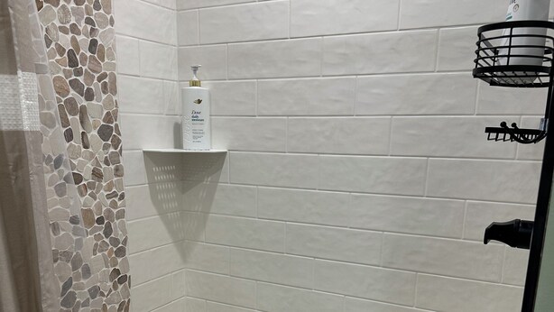 Douchegedeelte met witte tegels, een mozaïek vloer van natuursteen en een plank met toiletartikelen.