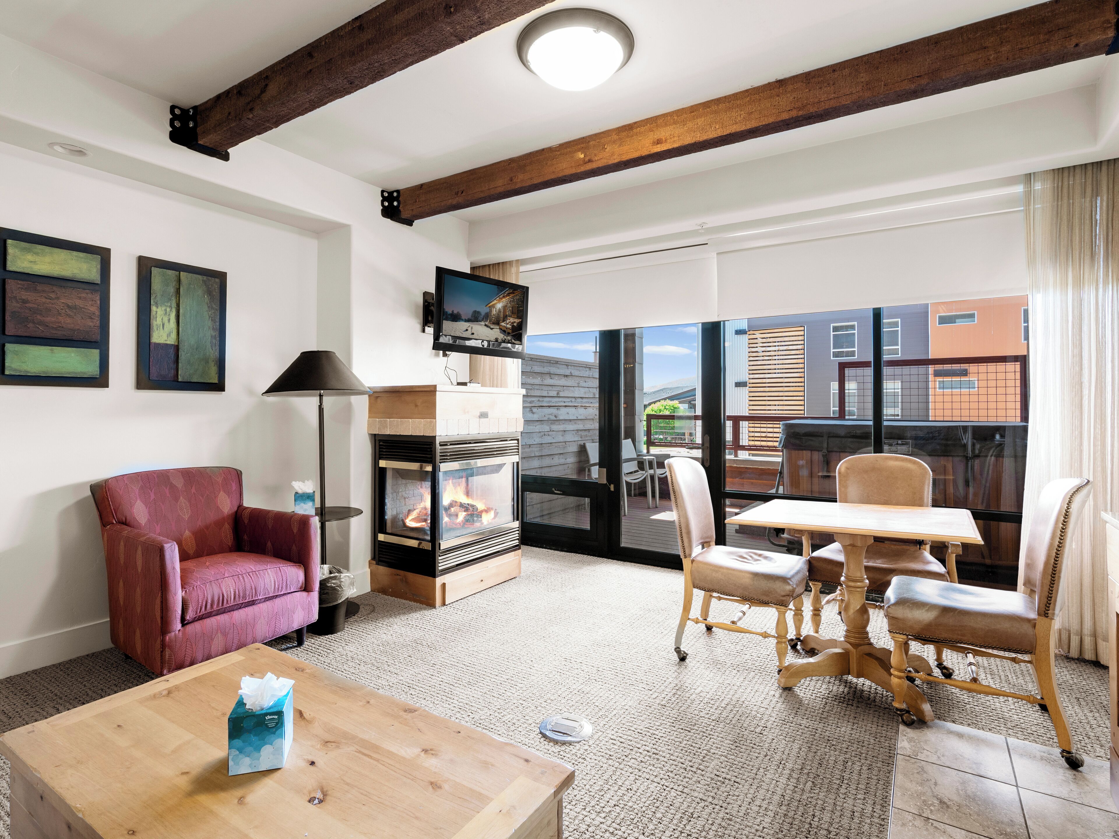 Una sala de estar acogedora con chimenea, un televisor montado encima y un balcón con vistas a edificios.