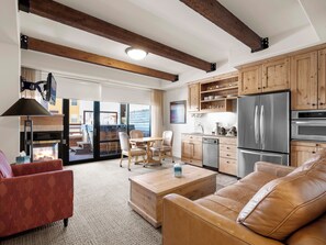 A modern kitchen with wooden cabinets, stainless steel appliances, and a large window overlooking a deck.
