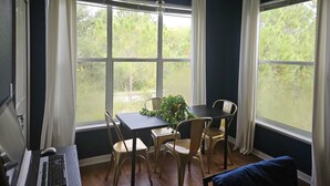 Ein Zimmer mit Schreibtisch, Stuhl und Tisch mit Sitzgelegenheiten. Ein Fenster bietet Blick auf grüne Umgebung.