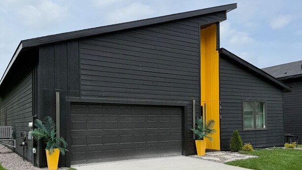 A modern two-story building with a dark exterior and a bright yellow door.