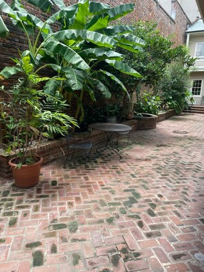 A brick patio with a table and chairs, surrounded by lush green plants and a brick wall.