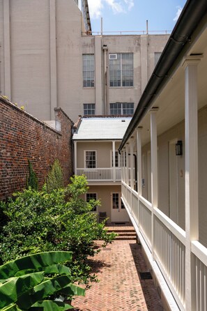 A narrow brick pathway leading to a building with a white exterior and a balcony.