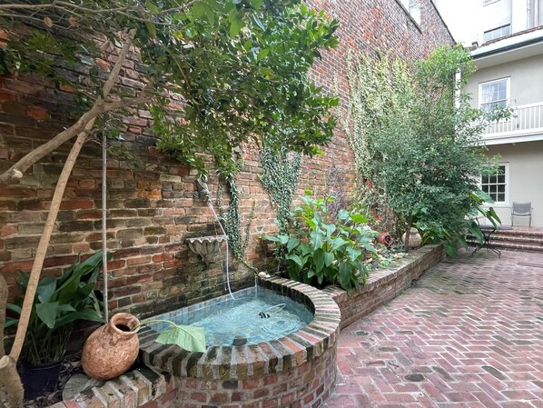 A brick courtyard with a small fountain, potted plants, and a brick wall.