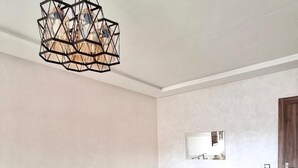 A modern dining room with a glass table and white chairs, a geometric chandelier, a large mirror, and a wooden door. - Winterized apartment (Marrakesh)