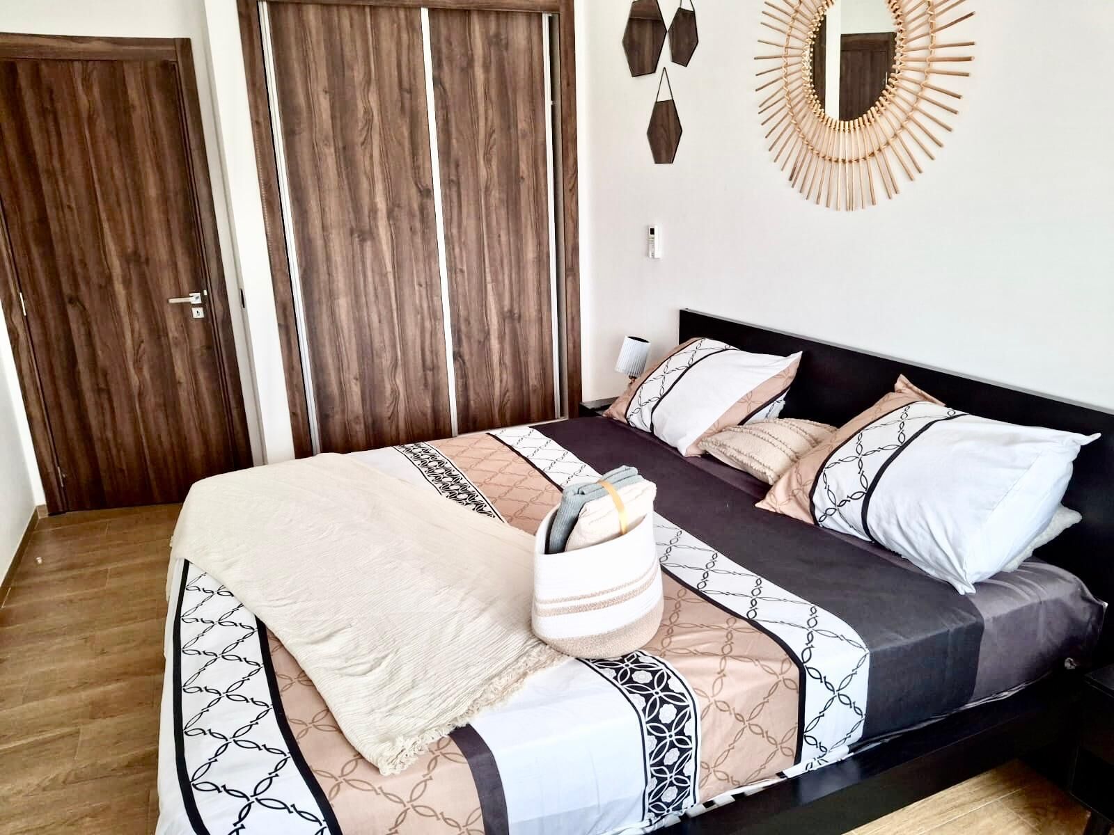 A bedroom with a bed, a bedside table, a wall-mounted mirror, and a wardrobe.