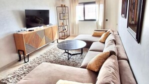 A modern living room with a sofa, coffee table, TV, and a decorative shelf. - Winterized apartment (Marrakesh)