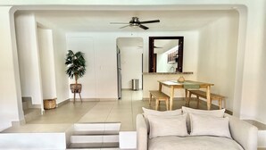 A modern living room with a sofa, a dining table with benches, a ceiling fan, and a staircase leading to another level. - Cancun House in Hotel Zone (Cancún)