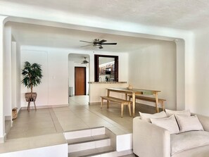 A modern living room with a sofa, a dining table with benches, a ceiling fan, and a staircase leading to another room. - Cancun House in Hotel Zone (Cancún)