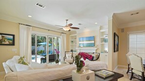 A spacious living room with a sofa, a coffee table, and a fireplace. There is a balcony with outdoor furniture and a view of the ocean. - Tropical Dreams by the Sea - Vacation Home with Private Pool & Close Proximity to Beach (Destin)