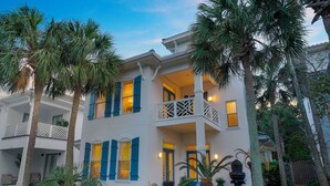 A two-story house with a balcony, surrounded by palm trees and potted plants. - Tropical Dreams by the Sea - Vacation Home with Private Pool & Close Proximity to Beach (Destin)