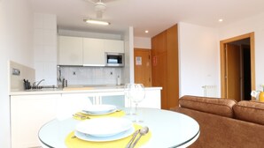 A modern kitchen with white cabinets, a microwave, and a dining area with a round glass table set for two. - APARTMENT LA BOLERA INDOOR BOWLING ALLEY (Llanes)