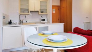 A compact kitchen with white cabinets, a microwave, and a dining table with yellow placemats. - APARTMENT LA BOLERA INDOOR BOWLING ALLEY (Llanes)