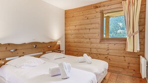 Ein Zimmer mit zwei Betten, Holzwänden, einem Fenster mit Vorhängen und einer Heizung.