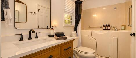 Une salle de bain avec un lavabo blanc, des robinets noirs, des meubles en bois, des toilettes blanches et une cabine de douche.