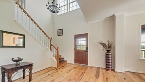 A spacious room with hardwood flooring, a wooden staircase, a large window, and a door with a decorative glass panel. - Luxury 90-acre 5BR Ranch near Cedar Creek (Kemp)