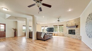 A spacious living room with hardwood flooring, a fireplace, a large TV, and a ceiling fan. - Luxury 90-acre 5BR Ranch near Cedar Creek (Kemp)