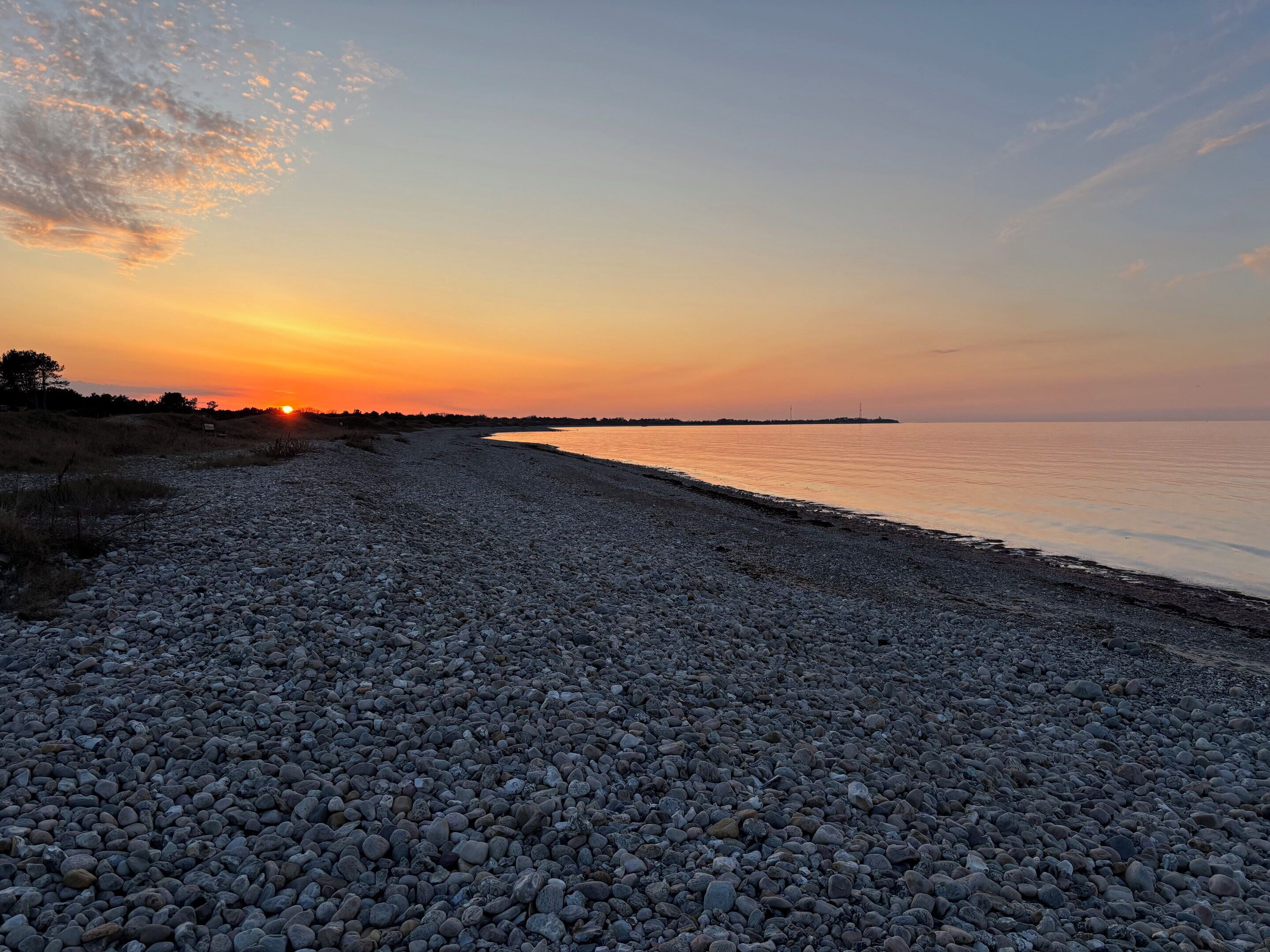 Une plage de galets avec un coucher de soleil en arrière-plan.