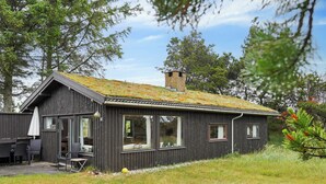 A wooden cabin with a sloped roof, large windows, and a small chimney. - Lovely cottage close to the North Sea (Pandrup)