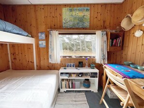 A wooden room with a bunk bed, a desk with books, a window with curtains, and a poster on the wall.
