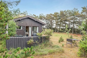 Une cabane dotée d’une terrasse, d’un coin repas et d’un petit espace extérieur aménagé pour s’asseoir.