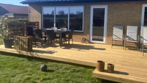 Eine Terrasse mit Tisch und Stühlen, eine Holzterrasse und ein Backsteinhaus mit großen Fenstern.