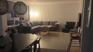 Ein modernes Wohnzimmer mit einem Ecksofa, einem Esstisch mit Stühlen, einem Couchtisch und einem Fernseher.