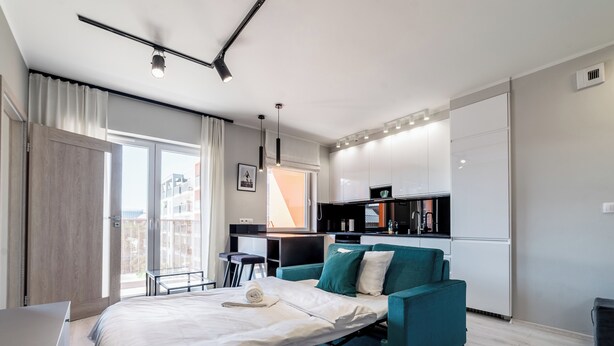 Una habitación de hotel moderna con cama, sofá color turquesa, escritorio y kitchenette.