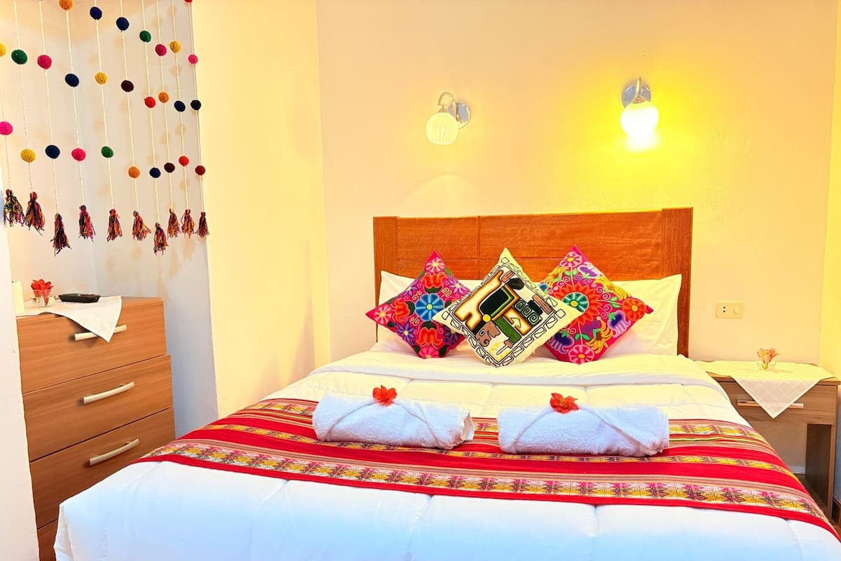 A neatly made bed with a red and white patterned bedspread, two decorative pillows, and a wooden headboard.
