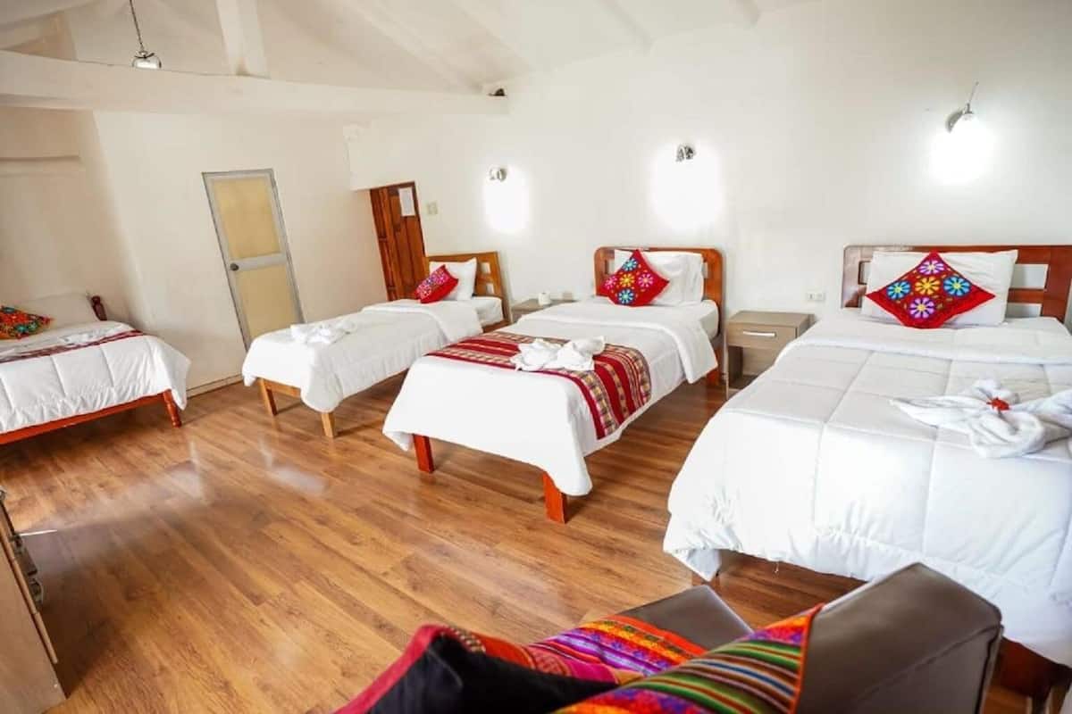A hotel room with three beds, wooden flooring, and a large window.