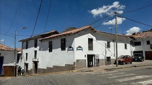 A white building with a tiled roof, a gated entrance, and a street with cars parked in front. - Hotel Horizonte Cuzco (Cusco)
