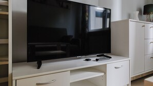 Een moderne woonkamer met een flatscreen televisie op een witte tv-meubel, een bank en een kast met lades.