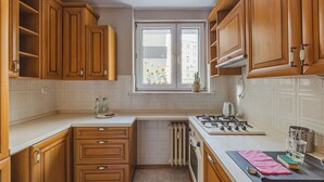 Een keuken met houten kastjes, een raam met uitzicht, een fornuis en een aanrecht met een waterkoker en een glas.